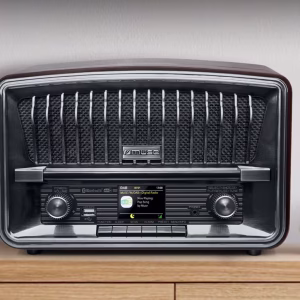 Una foto d'ambiente che mostra la radio M-135 DBT posizionata su un ripiano in cucina, con una tazza di caffè accanto. Il display è acceso su una stazione DAB+, comunicando calore, quotidianità e modernità.
