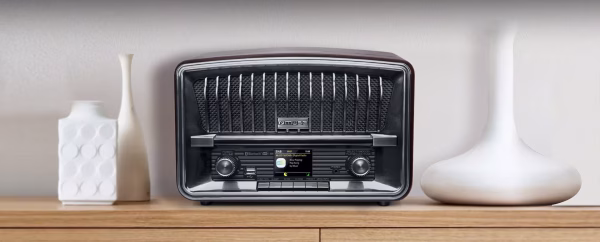 Una foto d'ambiente che mostra la radio M-135 DBT posizionata su un ripiano in cucina, con una tazza di caffè accanto. Il display è acceso su una stazione DAB+, comunicando calore, quotidianità e modernità.