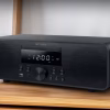Micro Hi-Fi Muse M-880 FBC completo, con l'unità centrale in alluminio e i due diffusori in legno, ambientato in un salotto moderno.