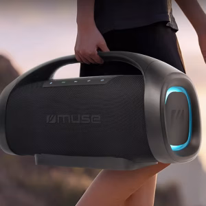 Un gruppo di amici in un giardino di sera si diverte attorno allo speaker Muse M-980 BT, che è al centro della scena con le sue luci multicolore che illuminano l'ambiente."